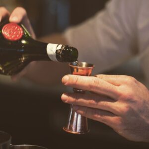 Bartending hands pouring dom benedictine into cobber jigger